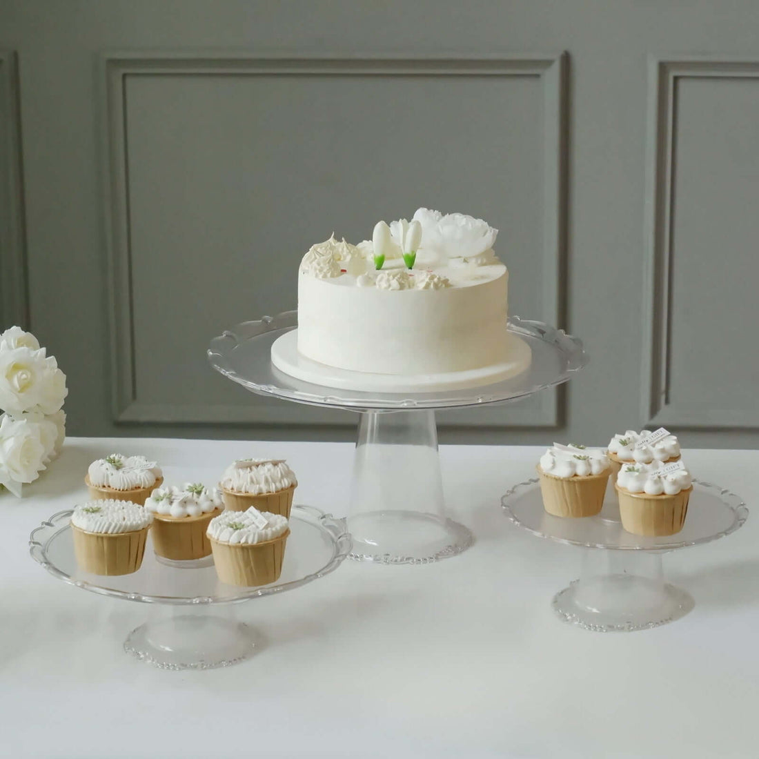 Elegant cake and cupcakes displayed on clear glass stands.