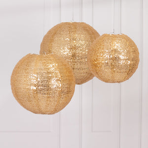 Three shimmering gold decorative lanterns hanging in a studio setting.