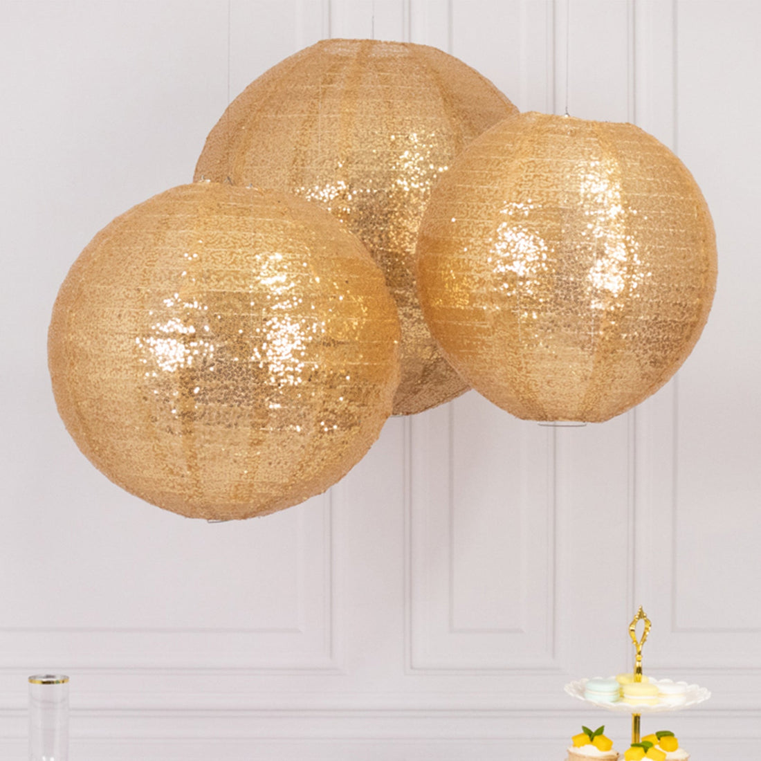 Three hanging gold sequin lanterns in a bright setting.