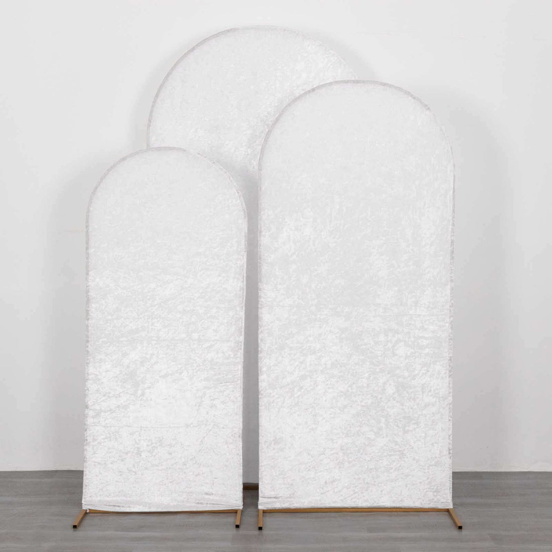 Three arched white fabric backdrops in varying heights on a plain surface.