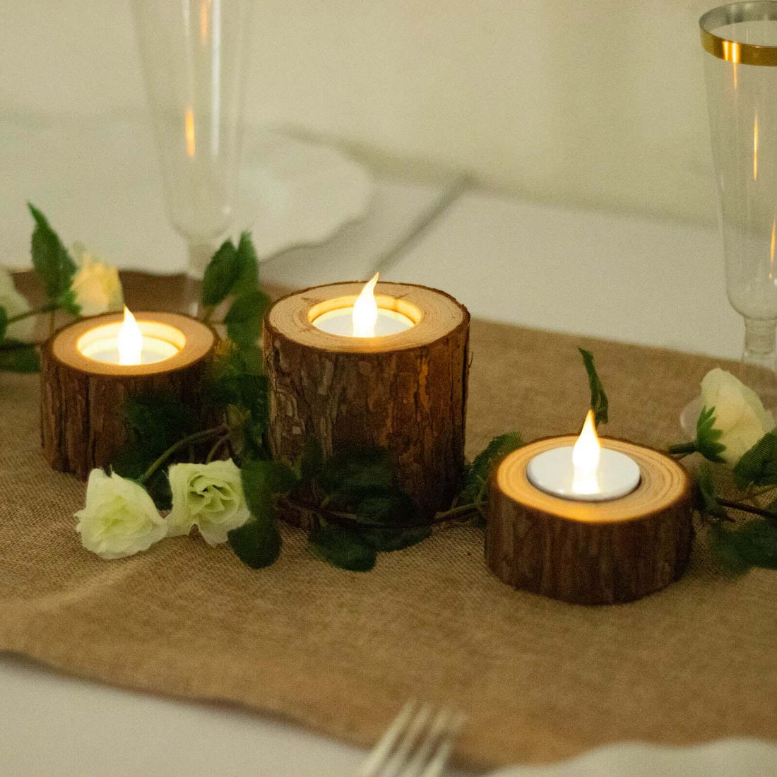 Wooden candle holders with tealights and greenery on a table setting.