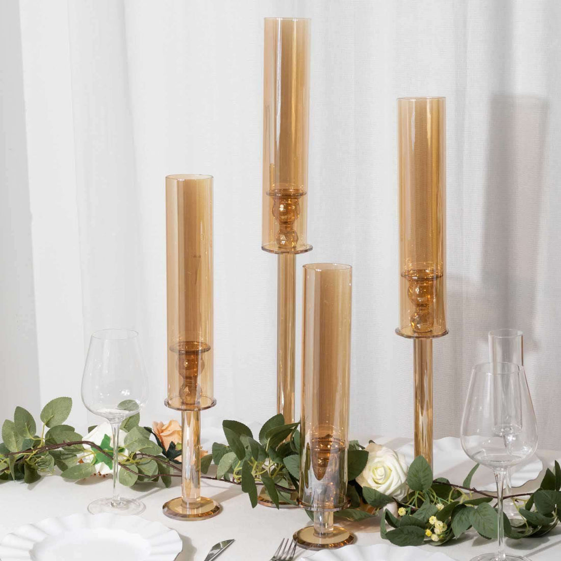 Elegant amber glass candle holders on a table with greenery and wine glasses.
