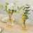 Elegant glass vases with flowers and greenery on a dining table.