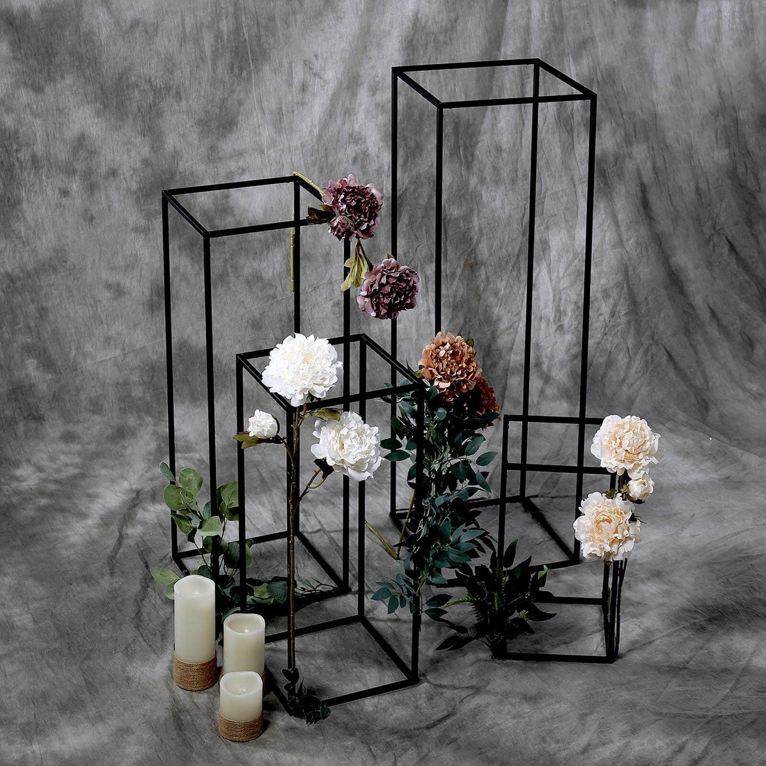 Decorative flower stands with blooms and candles on a textured gray backdrop.