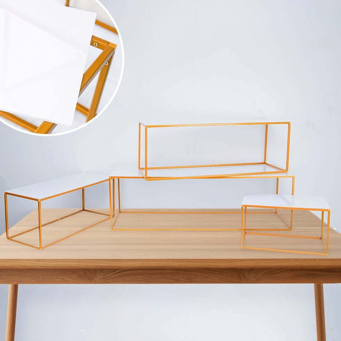 Geometric display stands with white surfaces and gold frames on a wooden table.