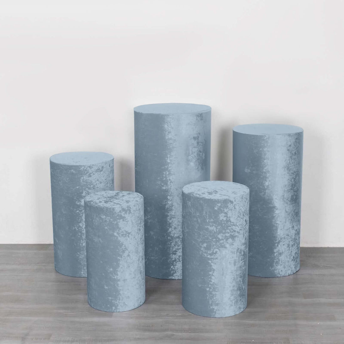Set of five blue velvet pedestals in varying heights on a neutral background.