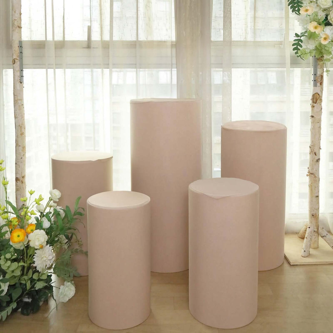 Set of five beige display pedestals in a bright, airy setting.