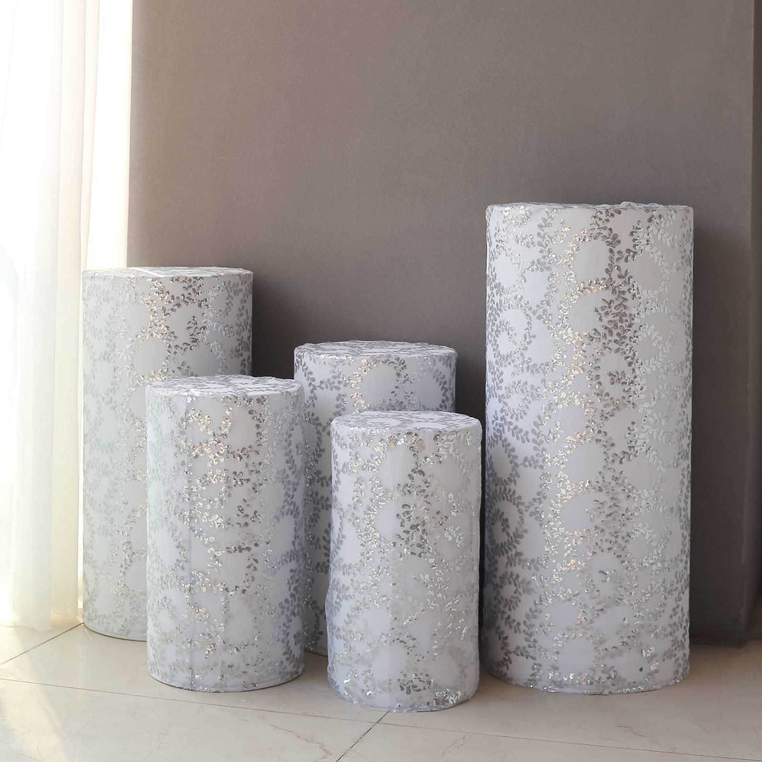 Decorative silver-patterned vases in various sizes against a neutral wall backdrop.