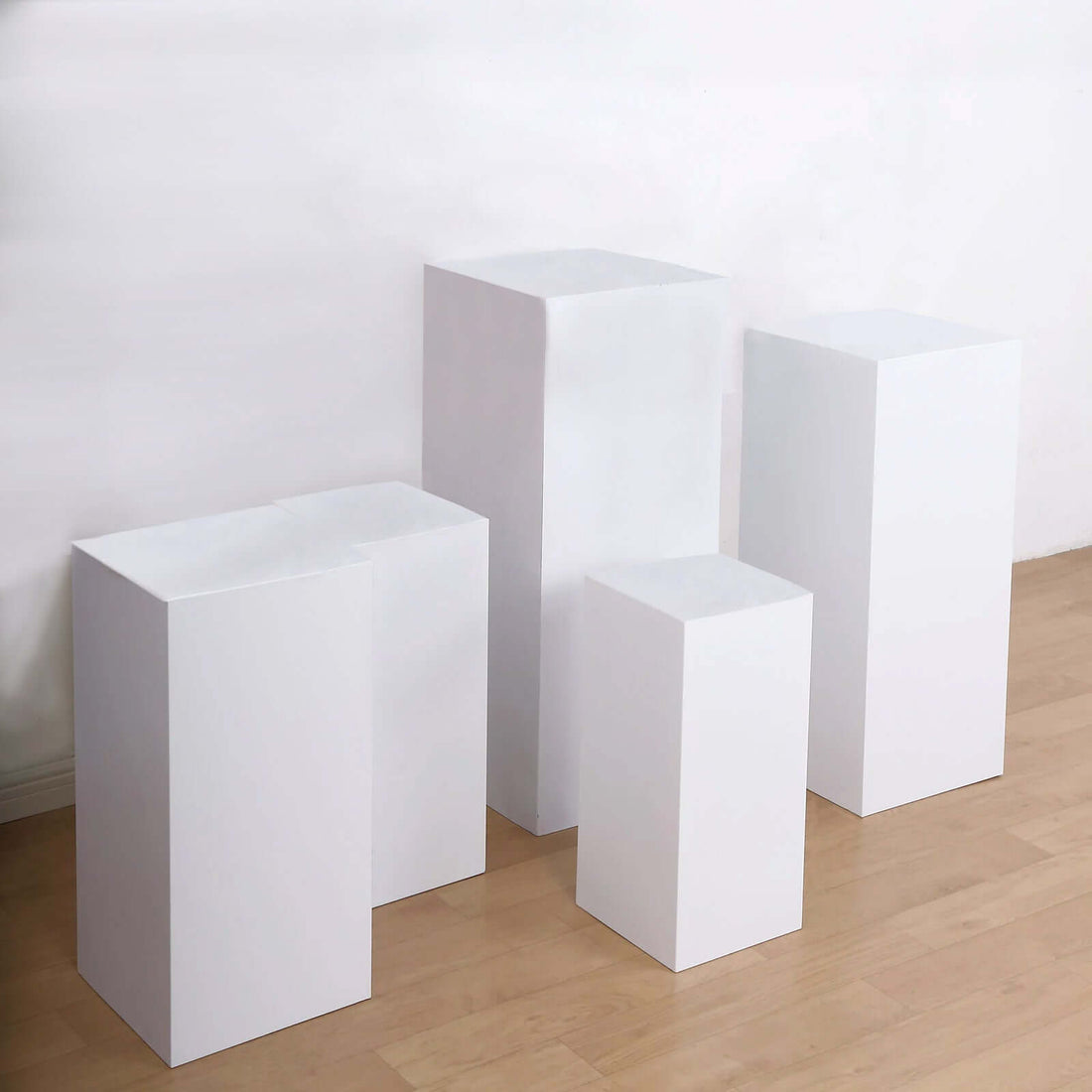 Set of four white display pedestals in various heights on a light wooden floor.
