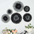 Black and gray decorative paper flowers arranged on a wall with plants in foreground.