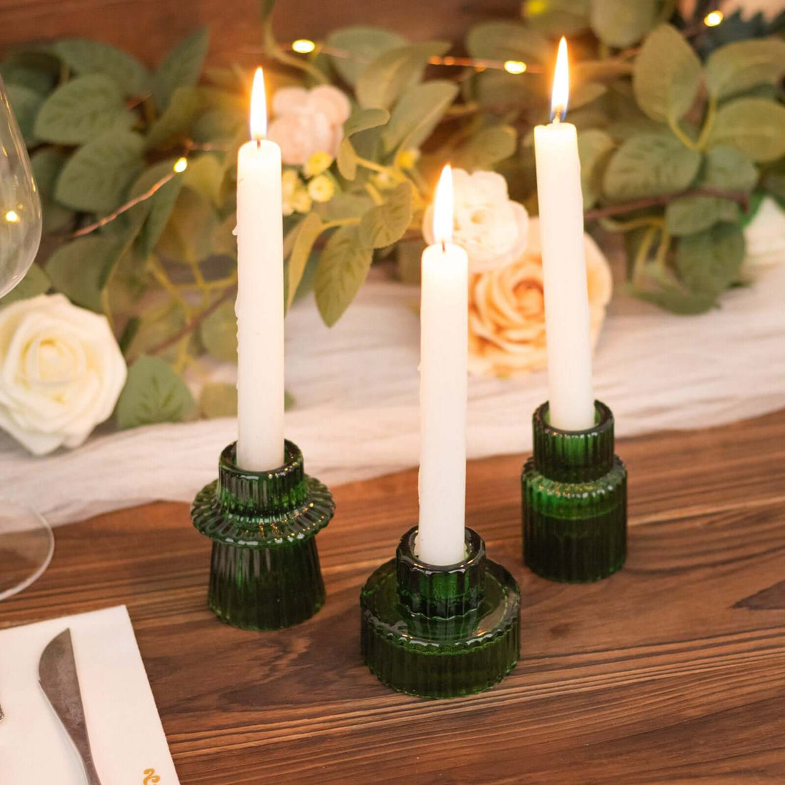 Green glass candle holders with white candles, elegantly displayed on a wooden table.