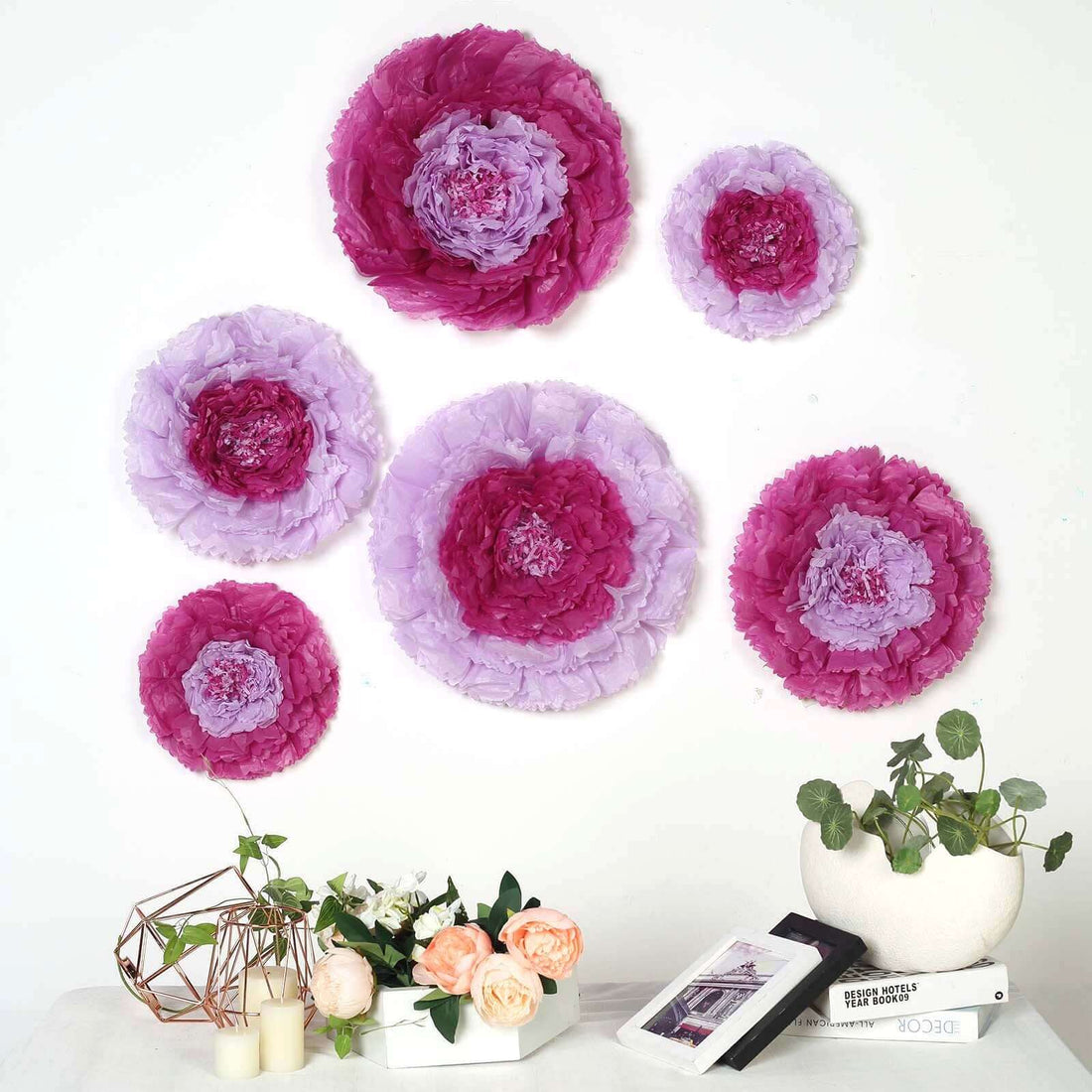 Colorful paper flowers arranged on a wall with floral decor and plants.