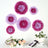 Colorful paper flowers arranged on a wall with floral decor and plants.