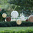 Decorative paper lanterns in various sizes hanging outdoors among greenery.