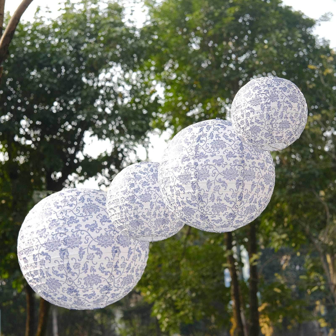 Decorative paper lanterns in varying sizes with blue patterns hanging outdoors.