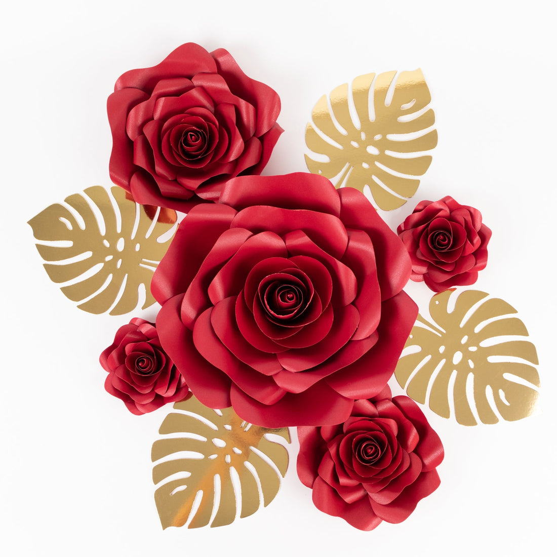 Red paper roses with gold monstera leaves on a white background.