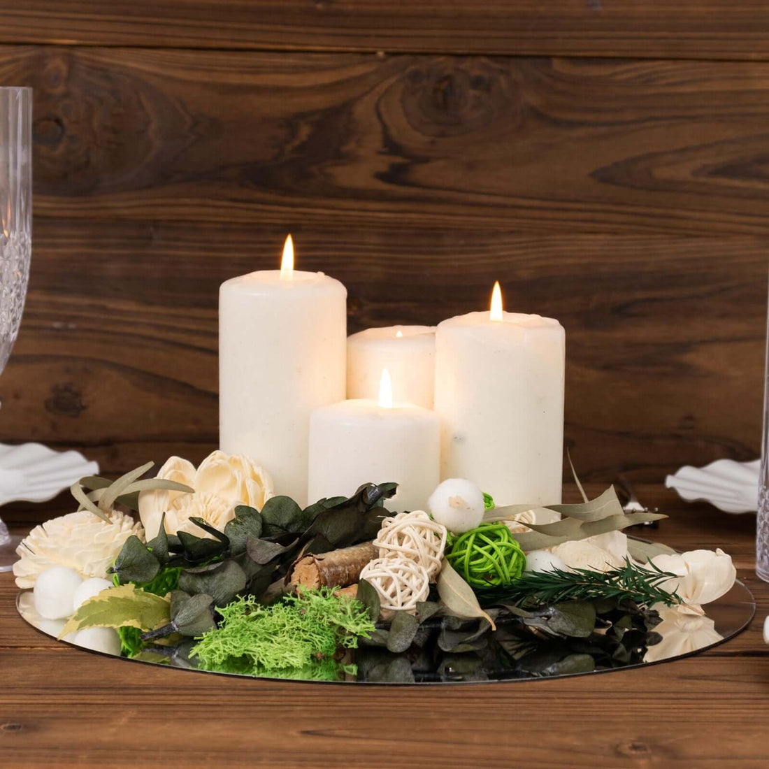 Decorative candle arrangement with greenery on a mirrored tray.