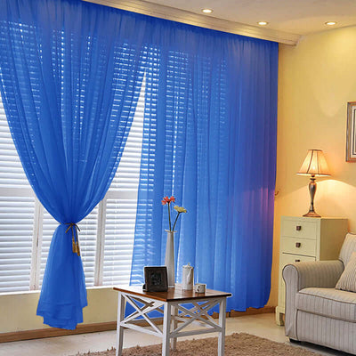Blue sheer curtains hanging in a cozy living room with a lamp and furniture.