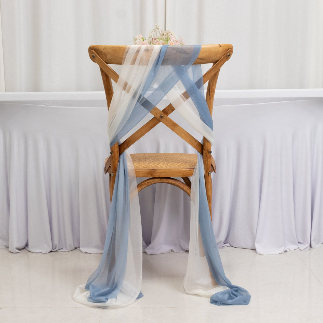 Wooden cross-back chair draped with blue and white sheer fabric.