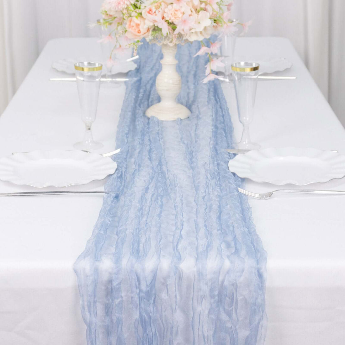 Light blue table runner on a white table set with elegant dinnerware and floral centerpiece.