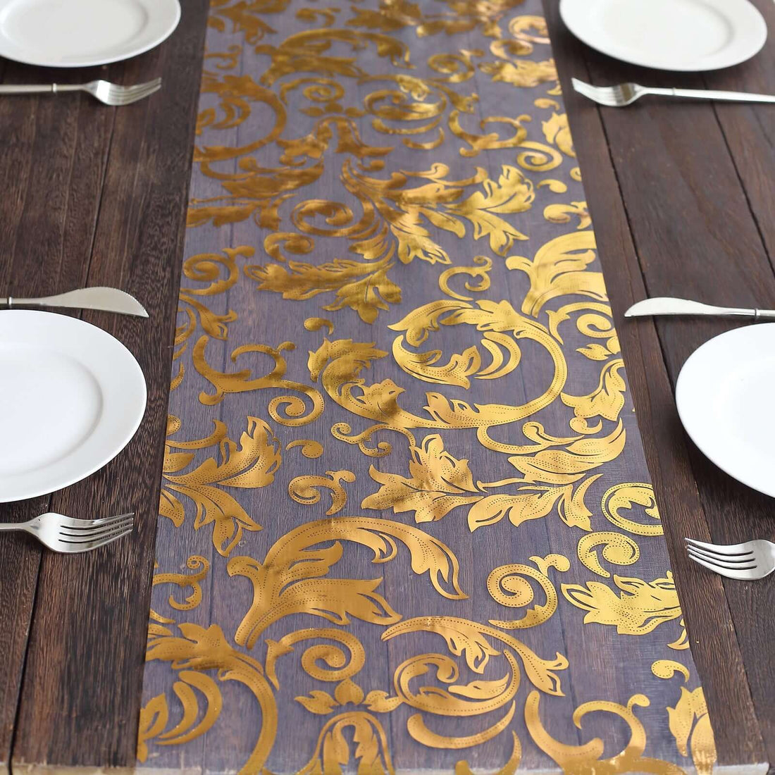 Elegant gold floral table runner on a rustic wooden table with plates and utensils.