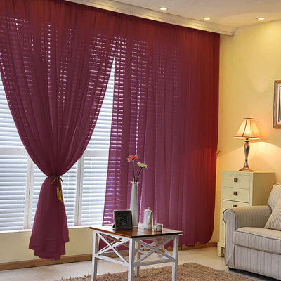 Sheer burgundy curtains hanging in a bright living room with a cozy sofa and lamp.