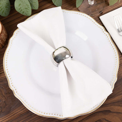 Elegant white plate with a folded napkin and silver napkin ring on a rustic table.
