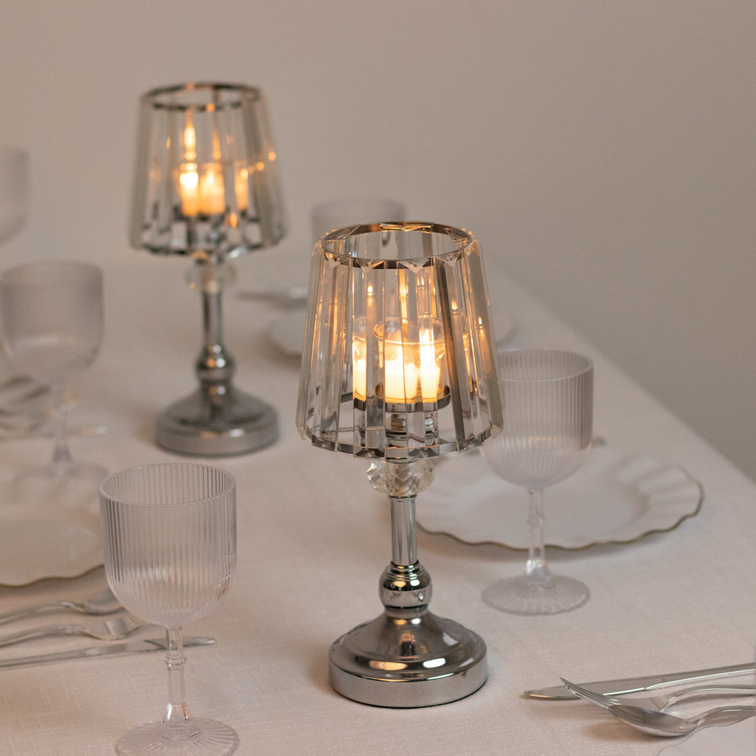 Elegant crystal candle holders with soft glowing candles on a dinner table setting.