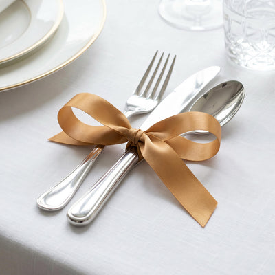 Silver cutlery tied with gold ribbon on a white elegant table setting