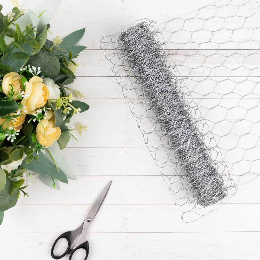 Wire mesh roll with scissors and floral arrangement on a wooden background.