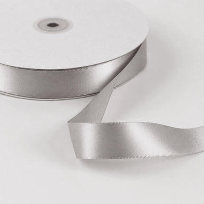 Silver satin ribbon roll on white background, close-up craft supply