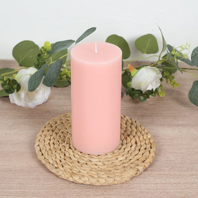 Pink pillar candle on a woven coaster with greenery accents.