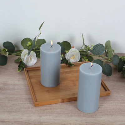 Gray pillar candles on a wooden tray with greenery and flowers.