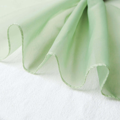 Green sheer fabric draped elegantly on a textured white surface.
