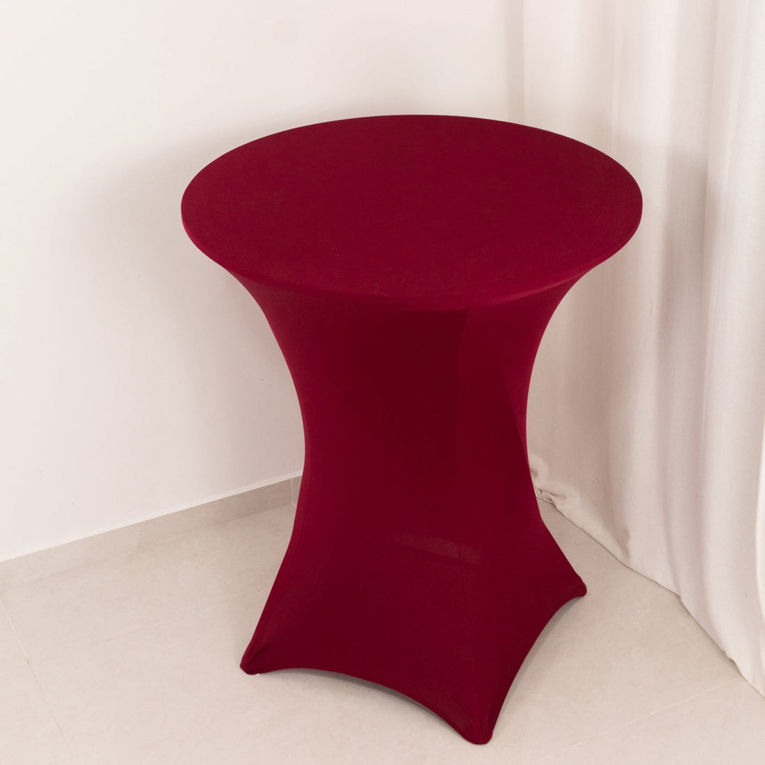 Round burgundy table with a fitted cover on a plain background.