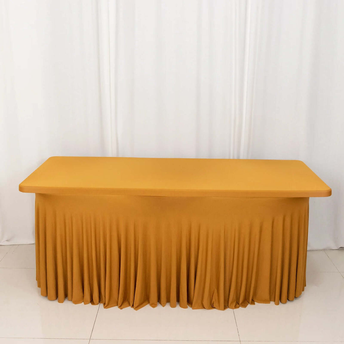 Yellow table with a pleated skirt on a plain backdrop.
