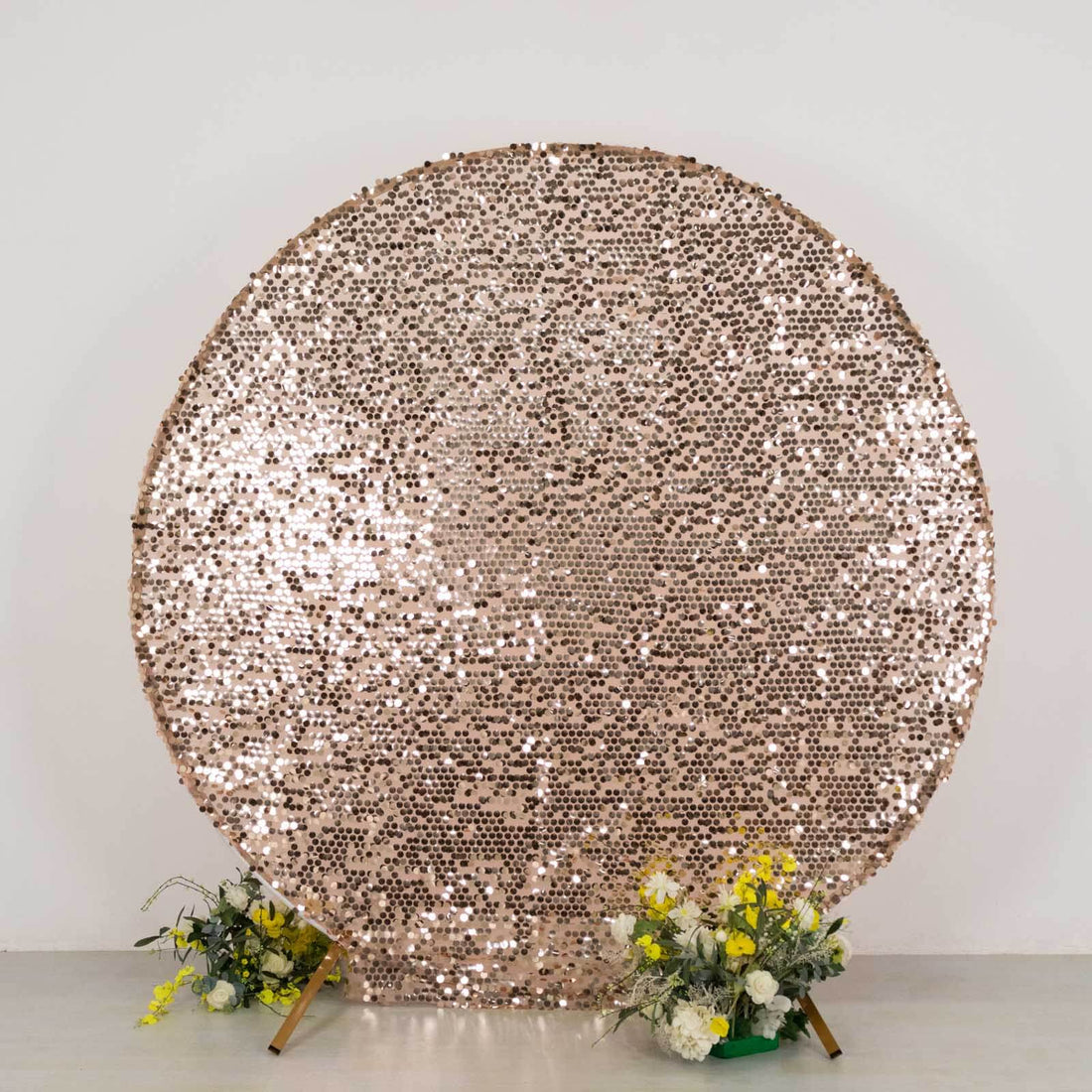 Rose gold sequin backdrop with floral arrangements at the base.