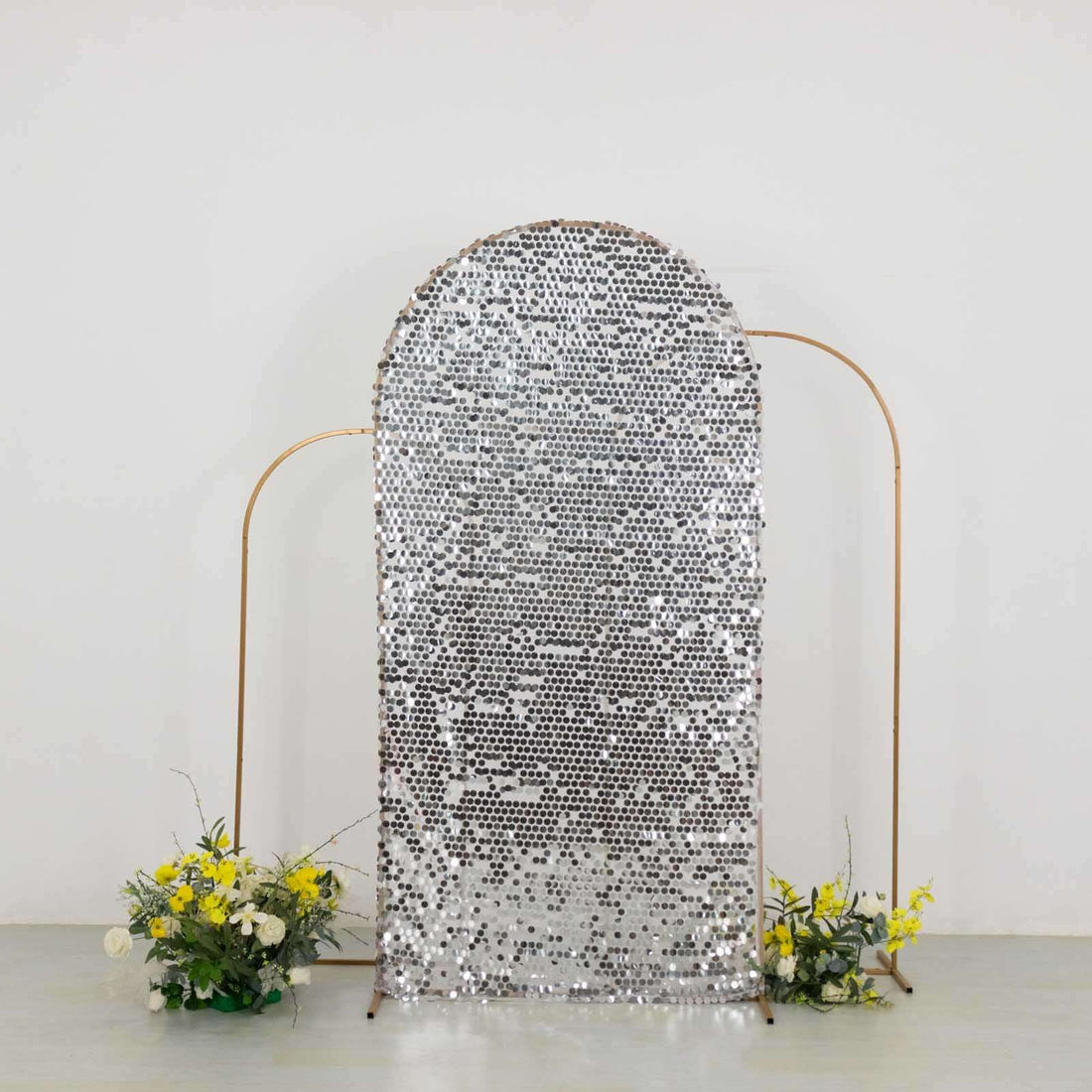 Silver sequin backdrop with floral arrangements on either side.