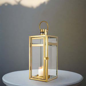 Gold metal lantern with glass panels and candle, styled on a table.