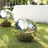 Reflective stainless steel garden orb on grass, showcasing outdoor ambiance.