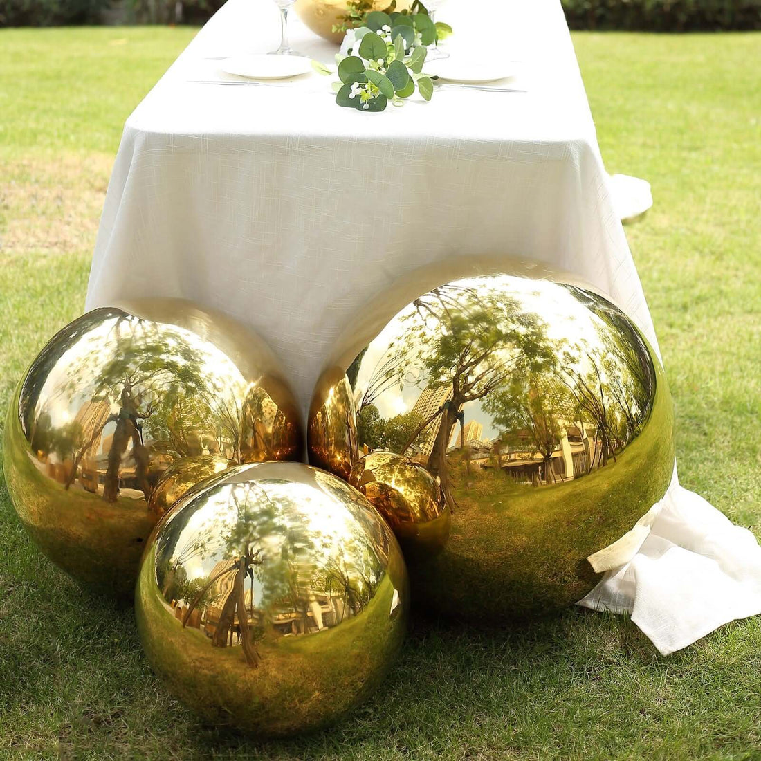 Gold decorative spheres on a table in a garden setting.