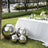 Decorative reflective spheres beside a table with flowers and glasses in a garden setting.