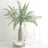 Decorative fern arrangement in a vase with plates and glasses on a table.