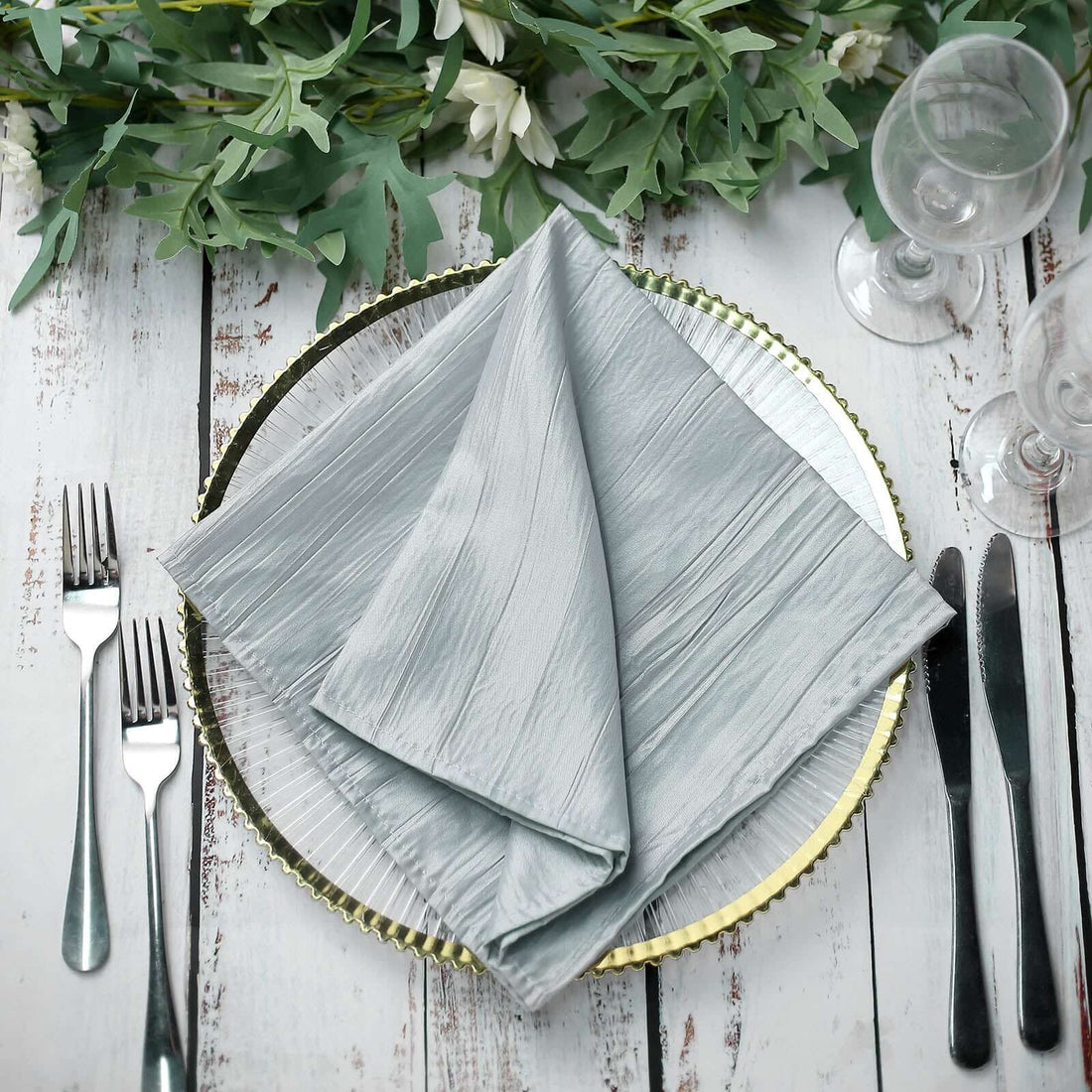 Elegant grey napkin folded on a decorative plate with cutlery and greenery. #whtbkgd