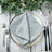 Elegant grey napkin folded on a decorative plate with cutlery and greenery. #whtbkgd