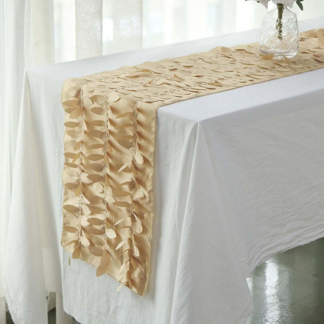 Beige satin table runner with leaf design on a white tablecloth.