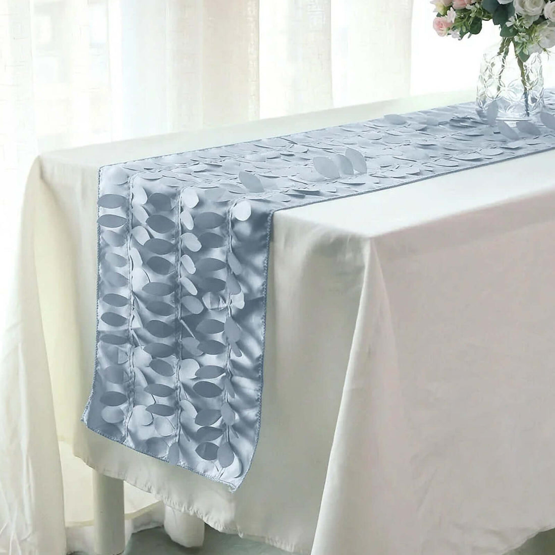 Elegant silver table runner with leaf design on a white tablecloth.