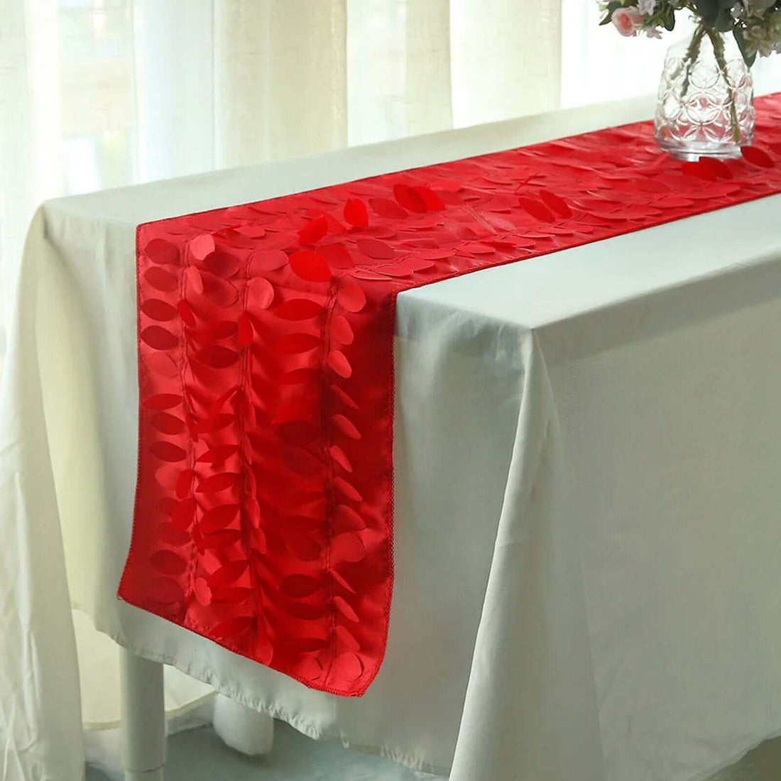 Red floral table runner on a white tablecloth with a vase of flowers.