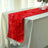 Red floral table runner on a white tablecloth with a vase of flowers.