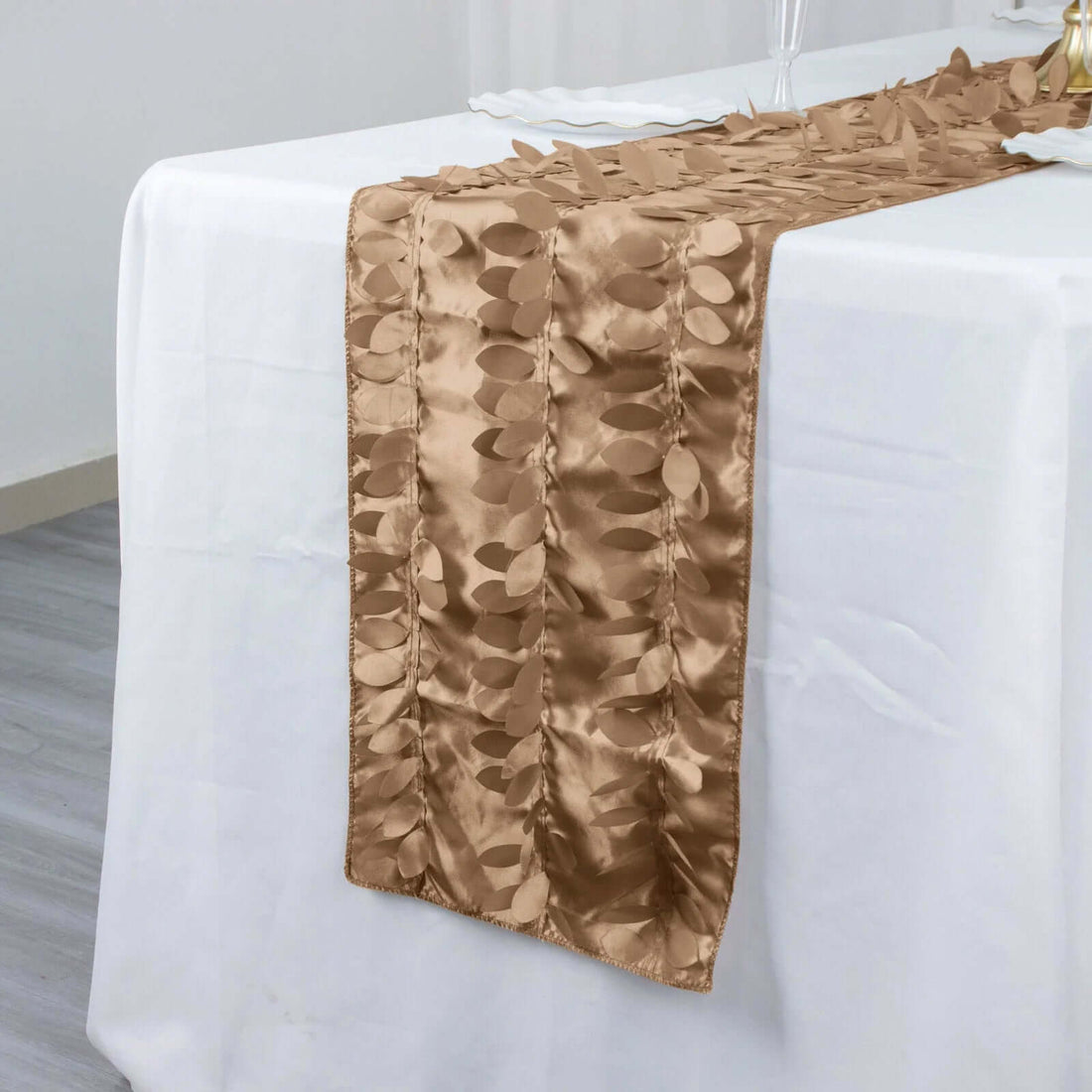Bronze table runner with textured leaf pattern on a white tablecloth.